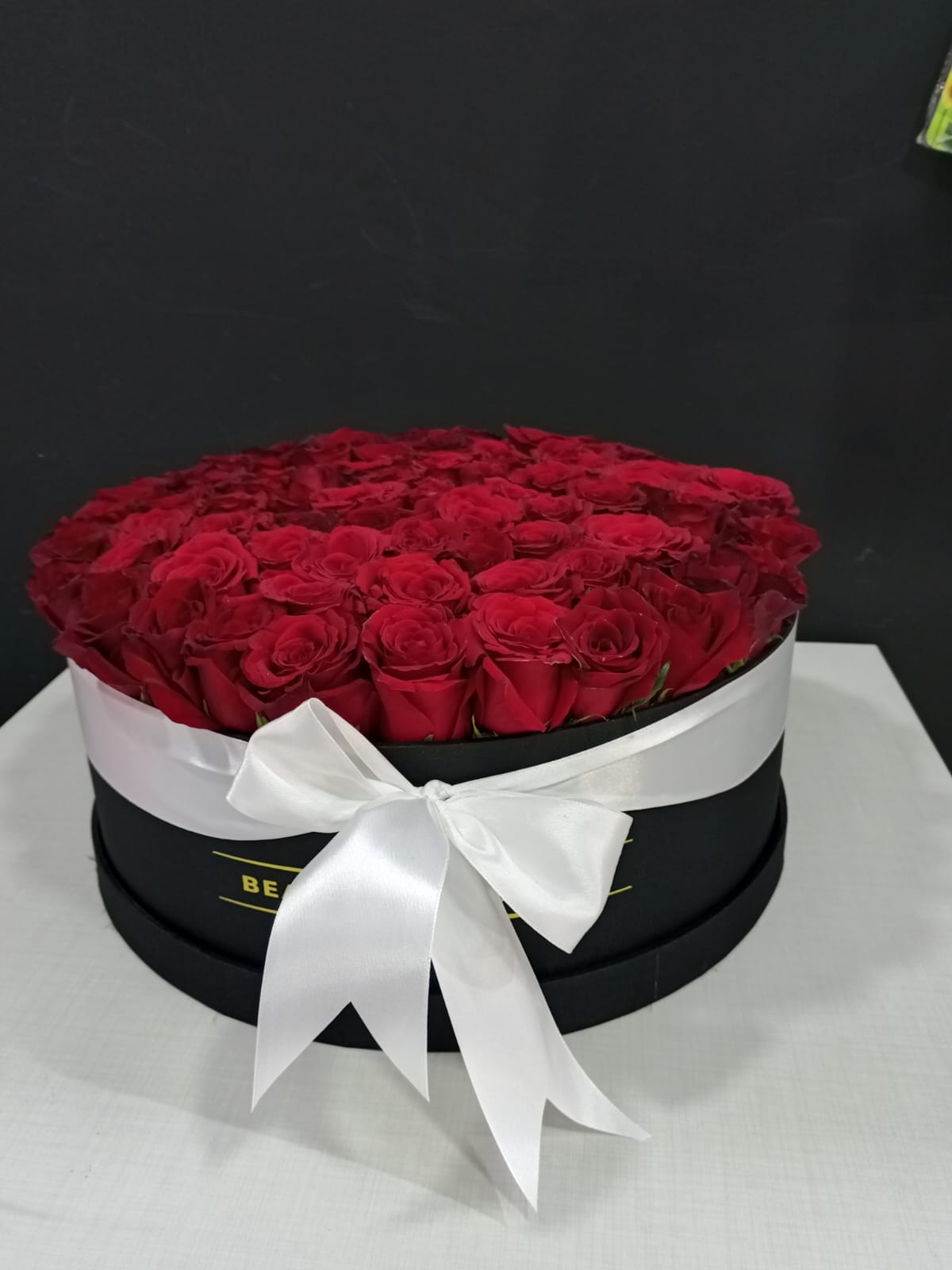 Round black box filled with red roses and white satin ribbon bow